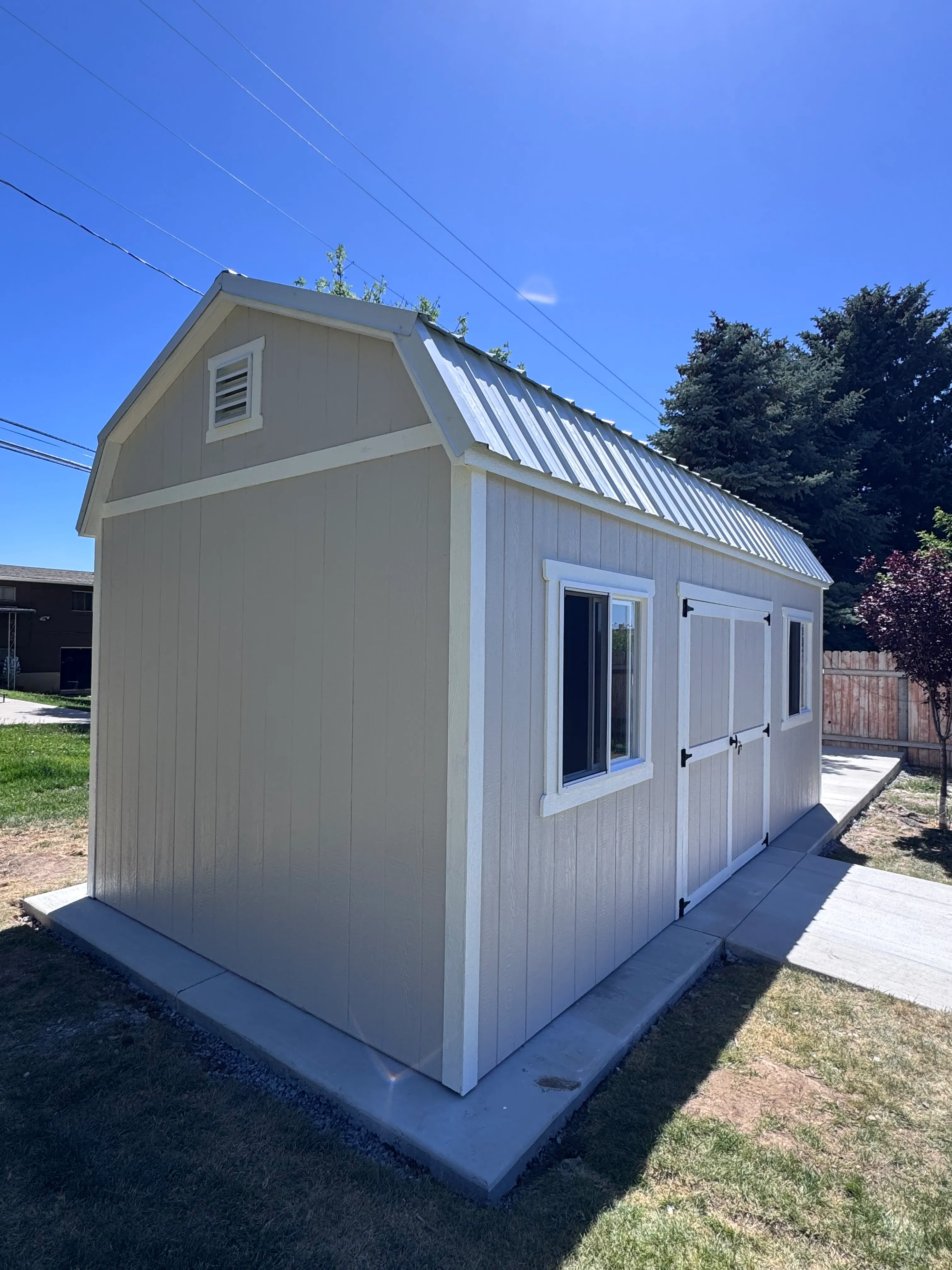 Tan barn style shed with metal roof on concrete pad by ShedPro LLC Utah